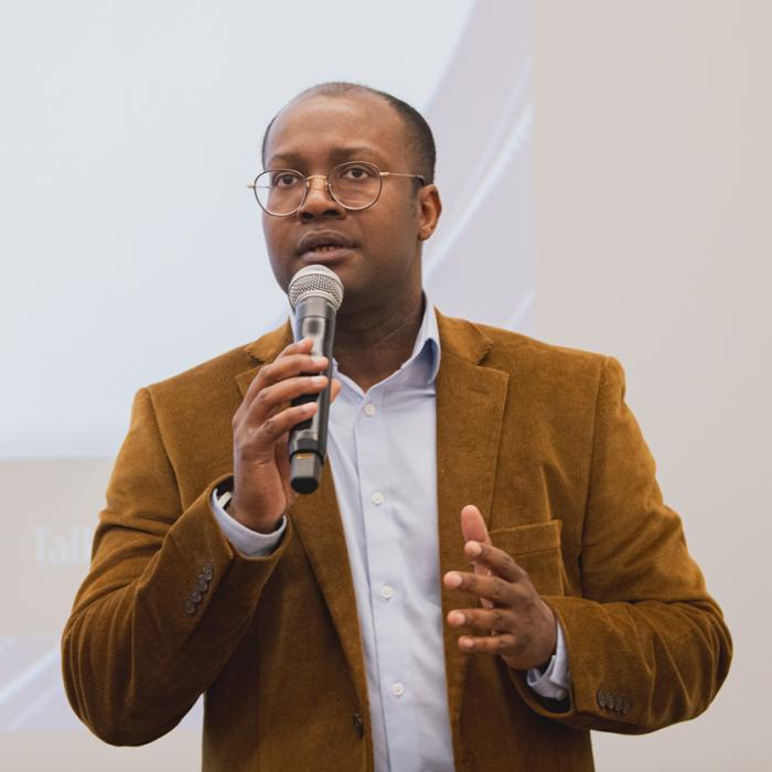 A man stands with a microphone as he addresses the audience at a college conference.