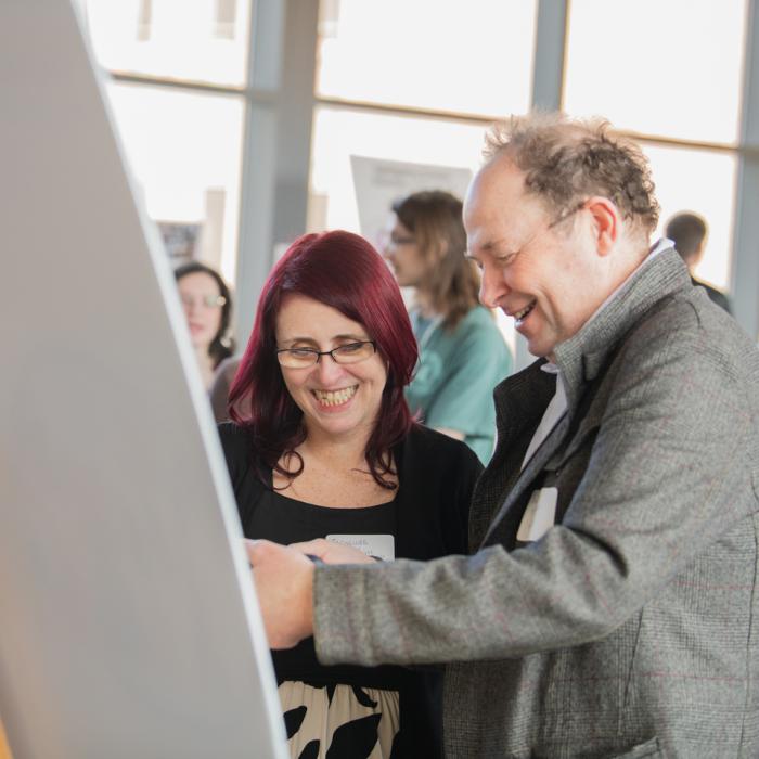A female faculty member on the left and a male faculty member looking at a poster and discussing their research.