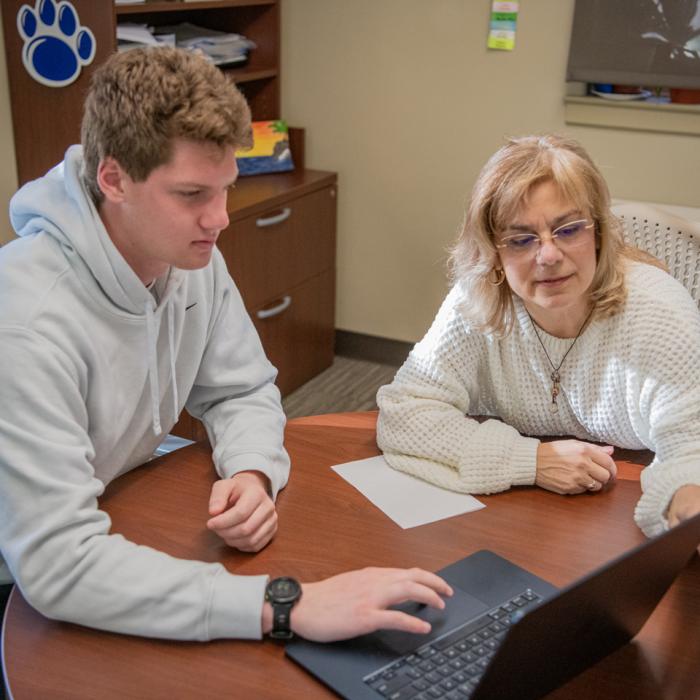 A biology adviser and an undergraduate student sitting at a table while looking at a computer screen.