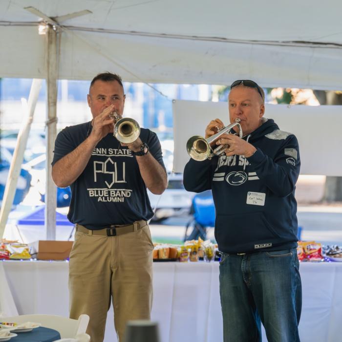 Two gentlemen in blue Penn State gear playing trumpets at the Penn State Homecoming tailgate.