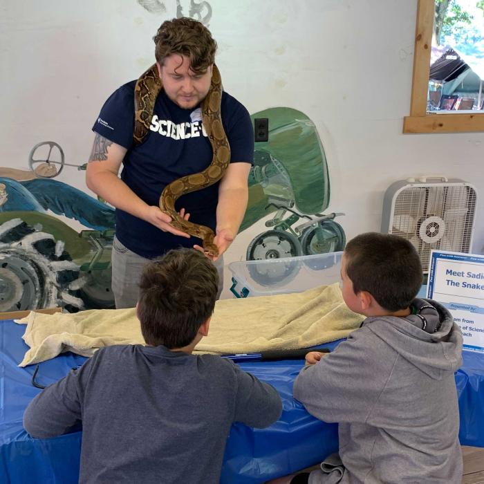 man in penn state shirt holds snake in front of kids