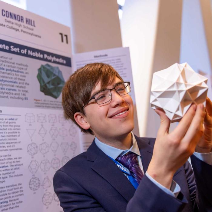 Connor Hill holding model of noble polyhedron in front of his research poster