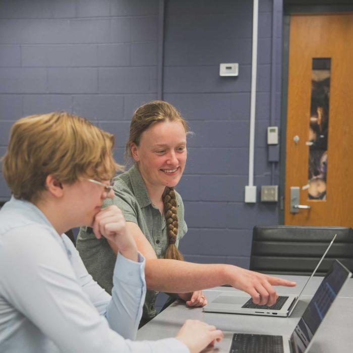 Charlotte Ward points at computer screen while grad student looks on