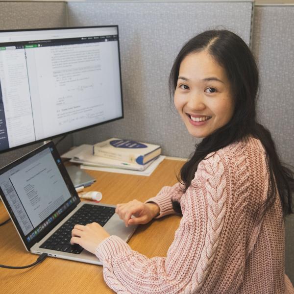 Postdoc Shurong Lin sits at a computer and looks at camera