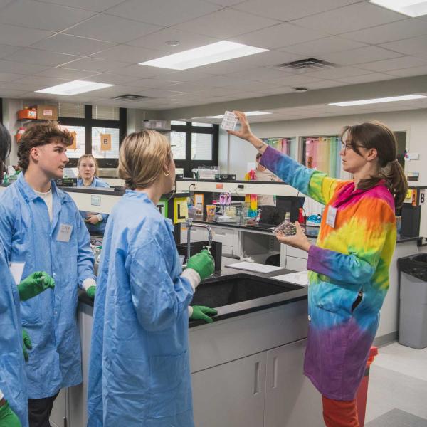 Carly Sjorgren shows lab sample to group of students wearing lab coats