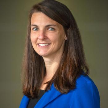 Picture of Katrina Merritt smiling in a blue blazer with a greenish gray background