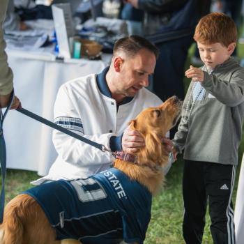  Alan Schaffranek and a child petting a golden retriever wearing a Penn State football jersey.