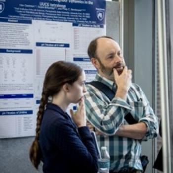Two attendees stand by research poster, reading and discussing data displayed on a scientific poster board.