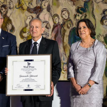 Jainendra Jain holding up the Wolf Prize plaque while posing for a photo with two other people.