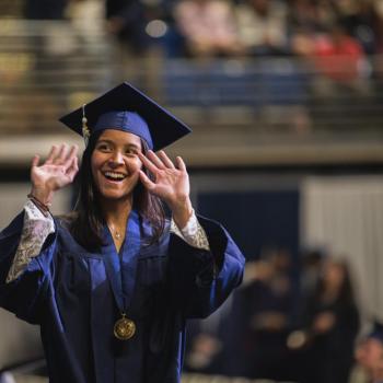 A coed student smiling and waving at the camera after she crosses the stage.
