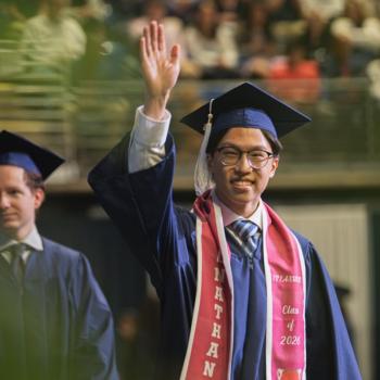 A student waving to his family in the audience as he walks across the stage.
