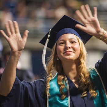 A coed student waves to her family in attendance as she returns to her seat.