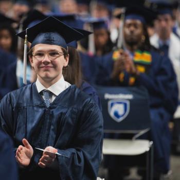 A sitting student smiles for a photo prior to the start of the commencement ceremony.