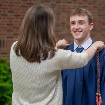 A proud parent arranges an honors sash or cord on her son.