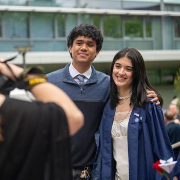 Two students smile while a family member takes a photo.