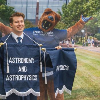 A future graduate poses in front of a display of the Nittany Lion Mascot.