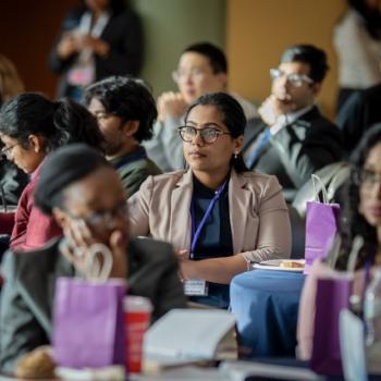 Audience members listening during a conference session at round tables.
