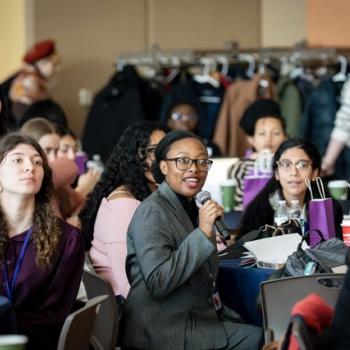 Audience members listening during a conference session at round tables.