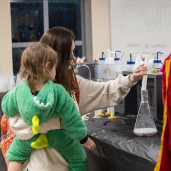 Haunted-U participant holding young child and observing science demo.