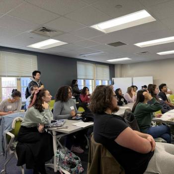 Group of people seated at a table with laptops, drinks, and snacks during an informal meeting or discussion.