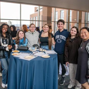 Small group poses around a standing table with food and materials at a campus networking event.
