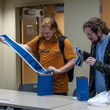 Two students standing at a table as the unfurl their college commencement stoles.